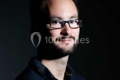 Structure en bois d'une halle éclairée par des lumières violettes, avec un toit en tuiles et des piliers en pierre.