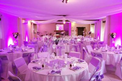 Structure en bois d'une halle éclairée par des lumières violettes, avec un toit en tuiles et des piliers en pierre.