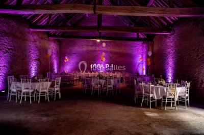 Structure en bois d'une halle éclairée par des lumières violettes, avec un toit en tuiles et des piliers en pierre.