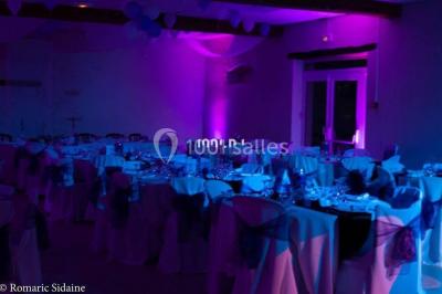 Salle voûtée avec colonnes en pierre, décorée de guirlandes végétales et éclairée par des lumières rouges et un DJ en…