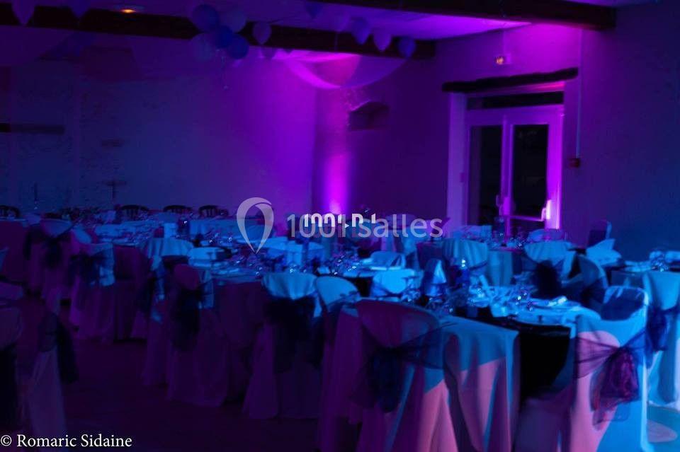 Salle de réception décorée avec des tables dressées et éclairage d'ambiance violet.