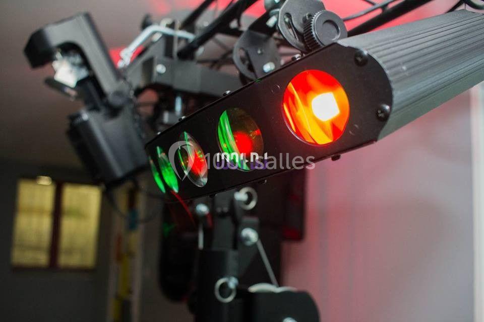 Projecteur lumineux avec faisceaux rouges et verts, monté sur une structure métallique dans un espace intérieur.