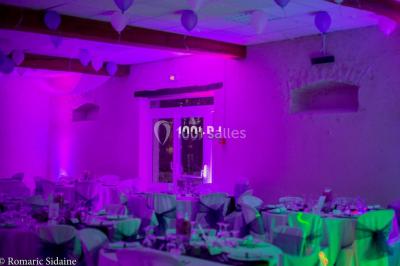 Salle voûtée avec colonnes en pierre, décorée de guirlandes végétales et éclairée par des lumières rouges et un DJ en…