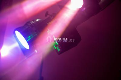 Salle voûtée avec colonnes en pierre, décorée de guirlandes végétales et éclairée par des lumières rouges et un DJ en…