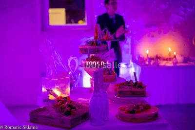 Salle voûtée avec colonnes en pierre, décorée de guirlandes végétales et éclairée par des lumières rouges et un DJ en…