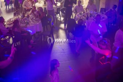 Salle voûtée avec colonnes en pierre, décorée de guirlandes végétales et éclairée par des lumières rouges et un DJ en…