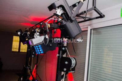 Salle voûtée avec colonnes en pierre, décorée de guirlandes végétales et éclairée par des lumières rouges et un DJ en…