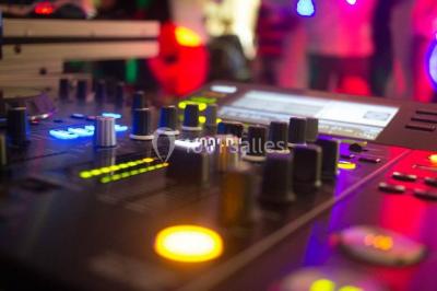 Salle voûtée avec colonnes en pierre, décorée de guirlandes végétales et éclairée par des lumières rouges et un DJ en…