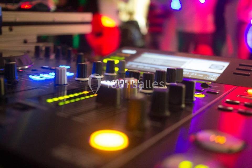 Table de mixage avec boutons et écrans lumineux dans une ambiance de soirée avec des lumières colorées en arrière-plan.