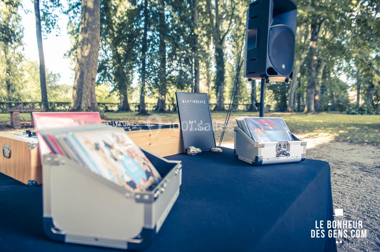 Table avec des bacs de vinyles, une enceinte et une table de mixage en extérieur, dans un parc arboré.