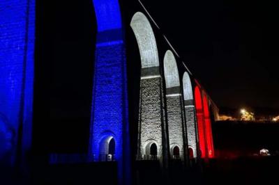 Salle voûtée avec colonnes en pierre, décorée de guirlandes végétales et éclairée par des lumières rouges et un DJ en…