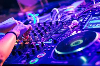 Salle voûtée avec colonnes en pierre, décorée de guirlandes végétales et éclairée par des lumières rouges et un DJ en…