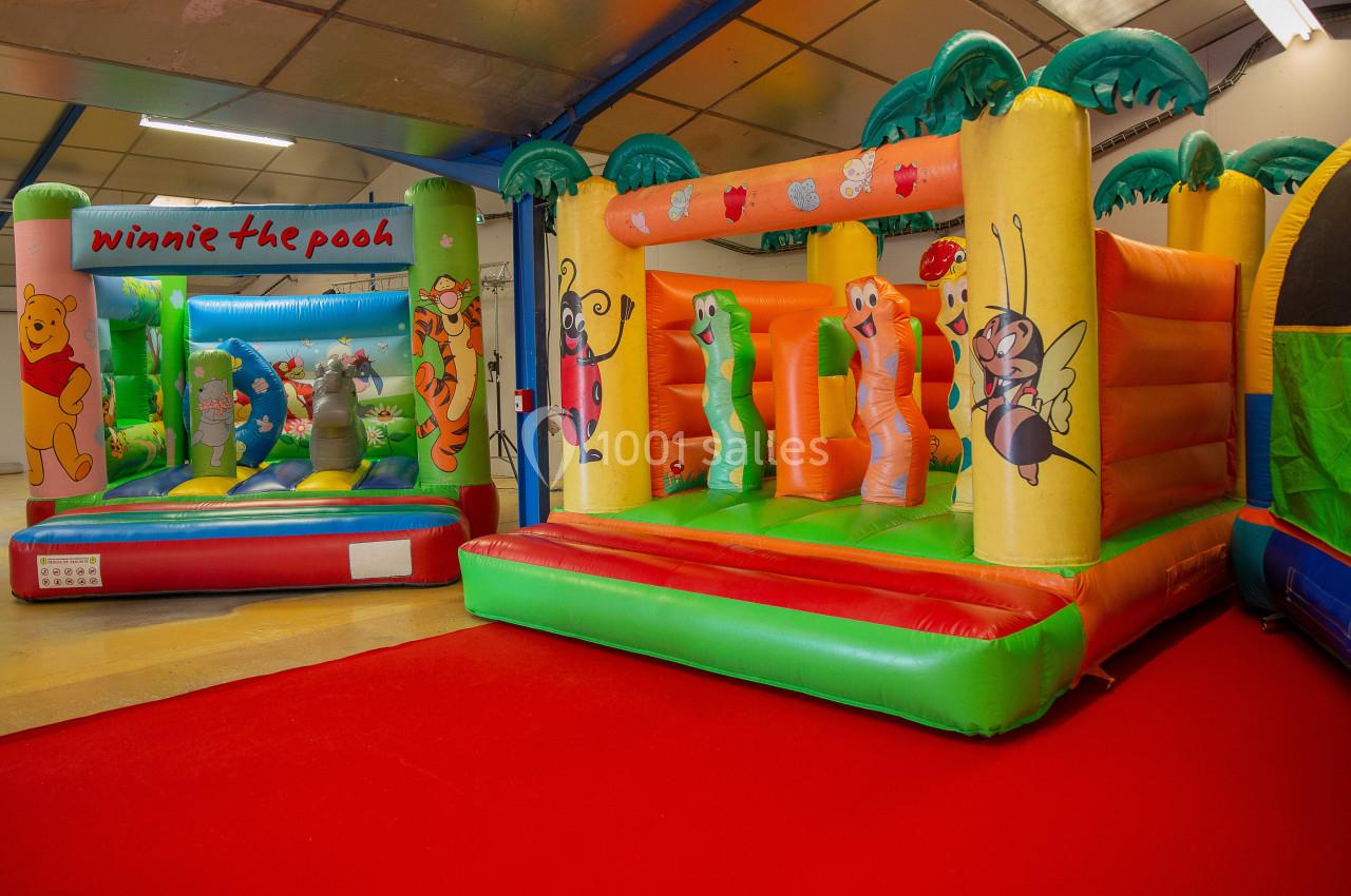 Deux structures gonflables colorées pour enfants, décorées de personnages et motifs ludiques, sur un sol rouge.