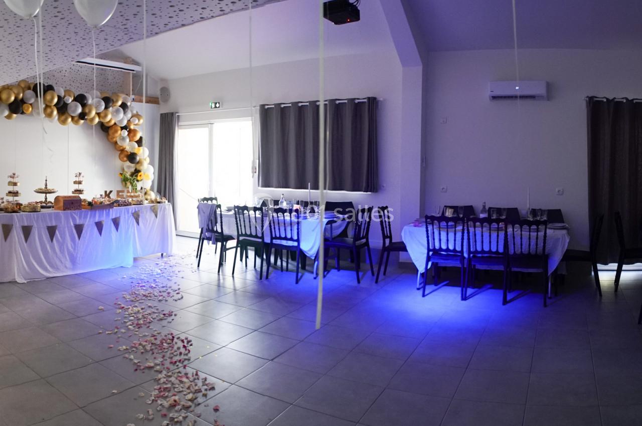 Salle décorée pour un événement avec tables dressées, guirlandes de ballons et pétales au sol.