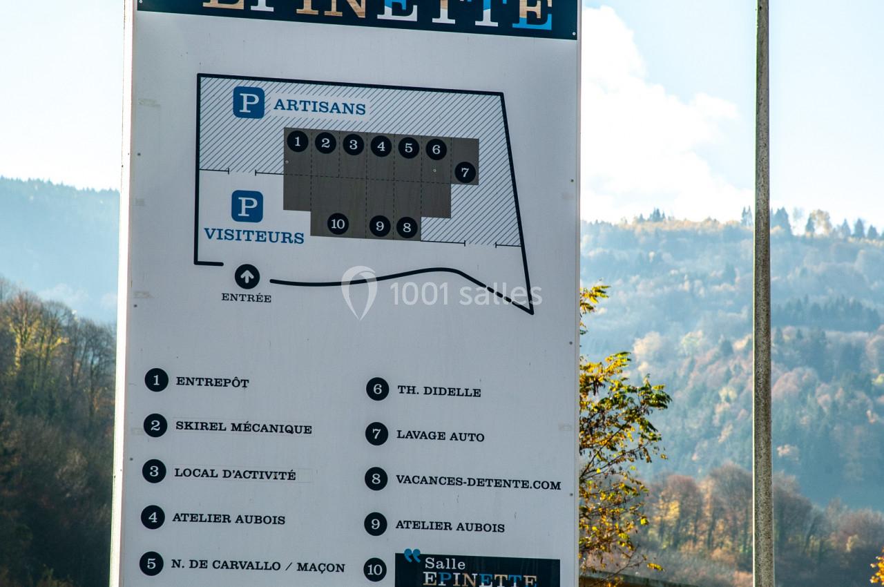 Panneau indiquant les services et parkings du bâtiment Épinette, avec un lampadaire et un paysage en arrière-plan.