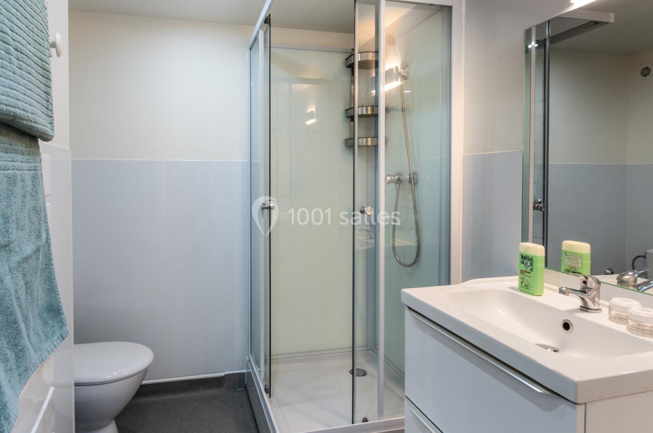 Salle de bain moderne avec douche vitrée, lavabo blanc avec miroir, toilettes et serviette suspendue.