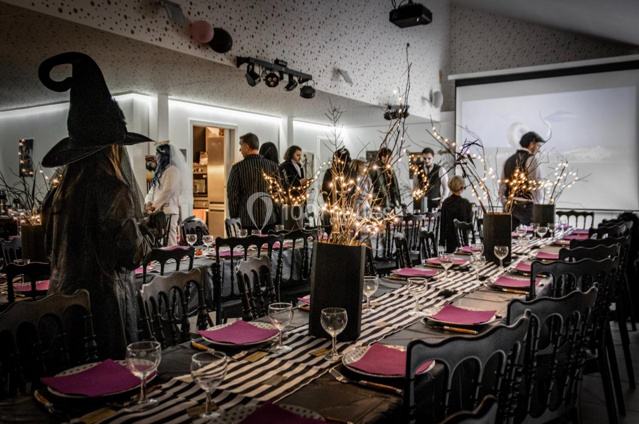 Salle décorée pour une fête avec des tables dressées, des lumières et des invités en costumes thématiques.