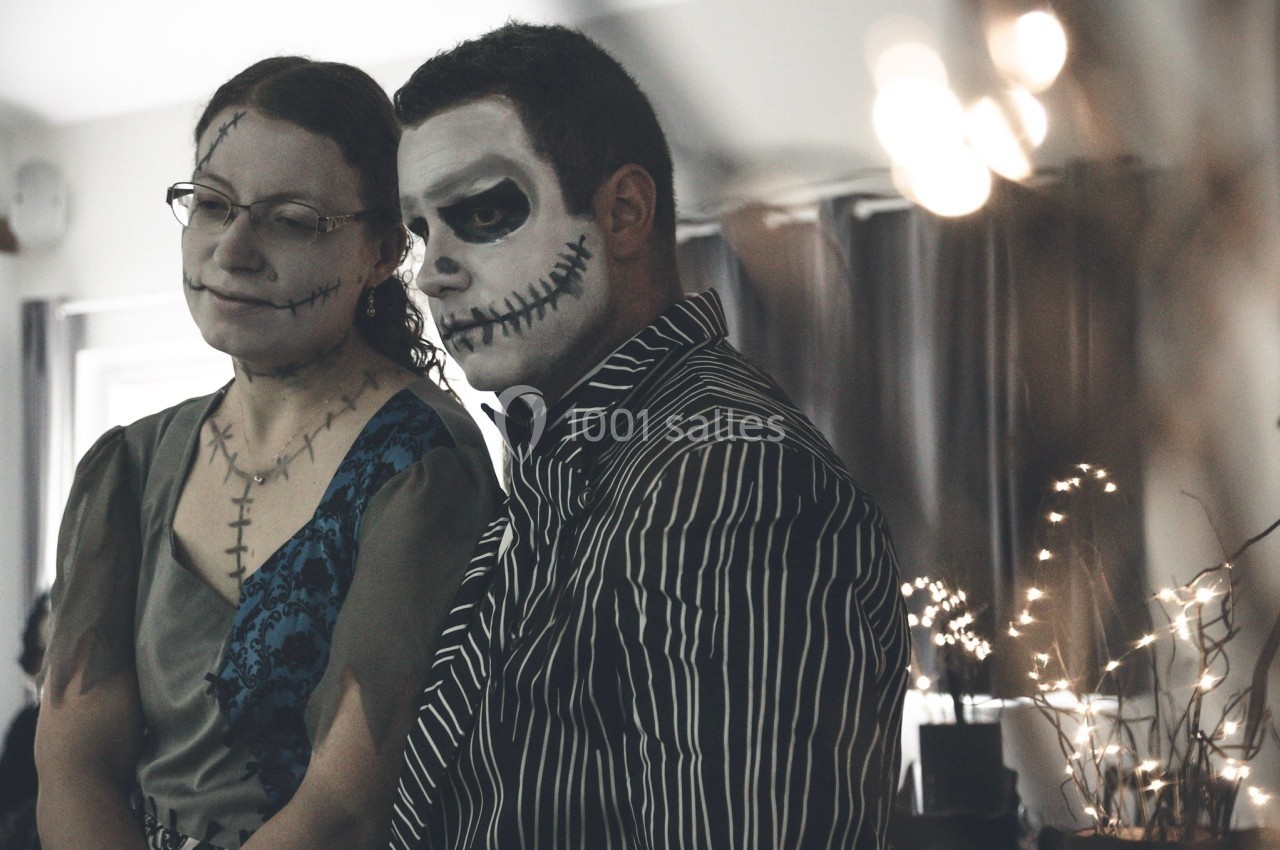 Deux personnes maquillées avec des motifs de crânes, debout dans une pièce faiblement éclairée avec des décorations…