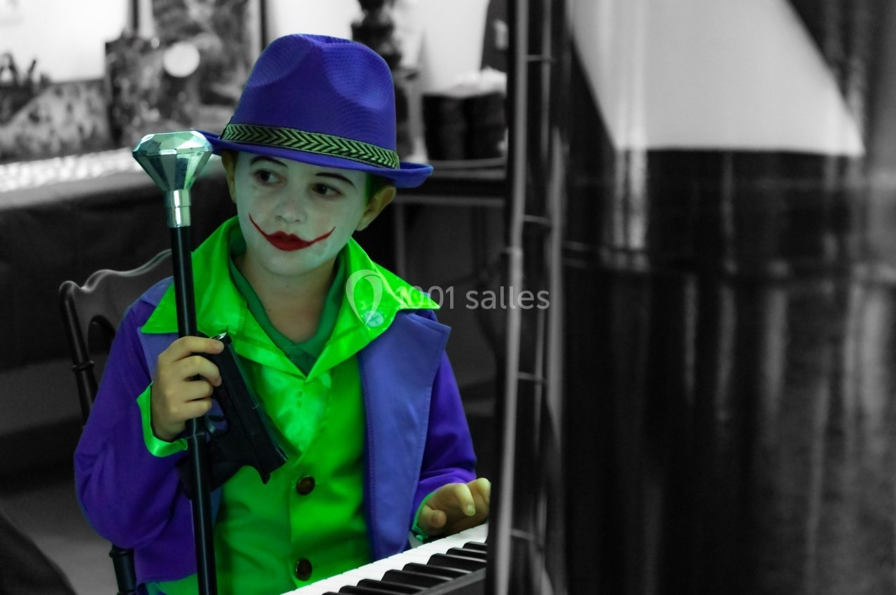 Un enfant déguisé en personnage de clown avec un chapeau violet, tenant un micro devant un clavier.