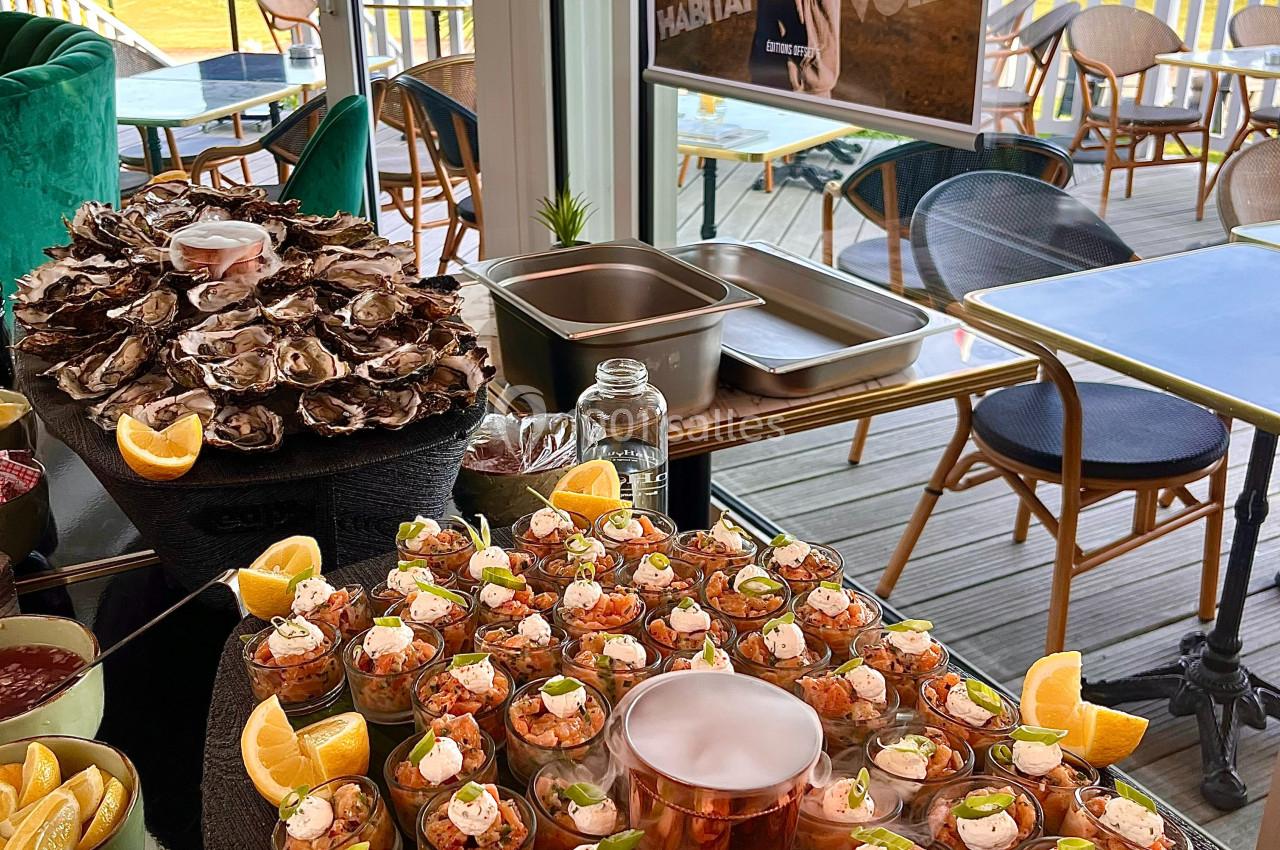 Buffet avec verrines de crevettes, huîtres et citrons, installé dans une salle lumineuse avec vue sur une terrasse.