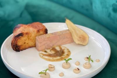 Assiette avec un bloc de foie gras, tranche de pain brioché, poire pochée et décorations de crème et noisettes.