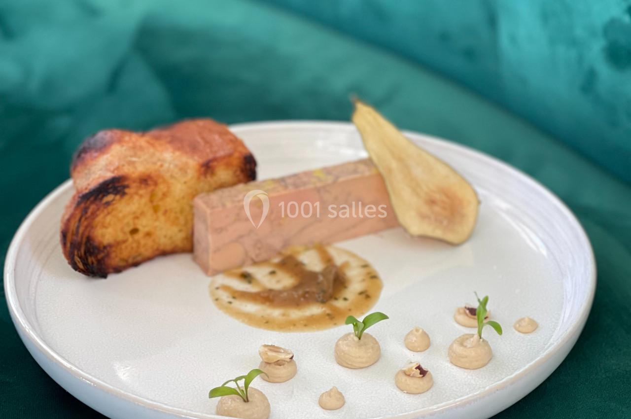 Assiette avec un bloc de foie gras, tranche de pain brioché, poire pochée et décorations de crème et noisettes.