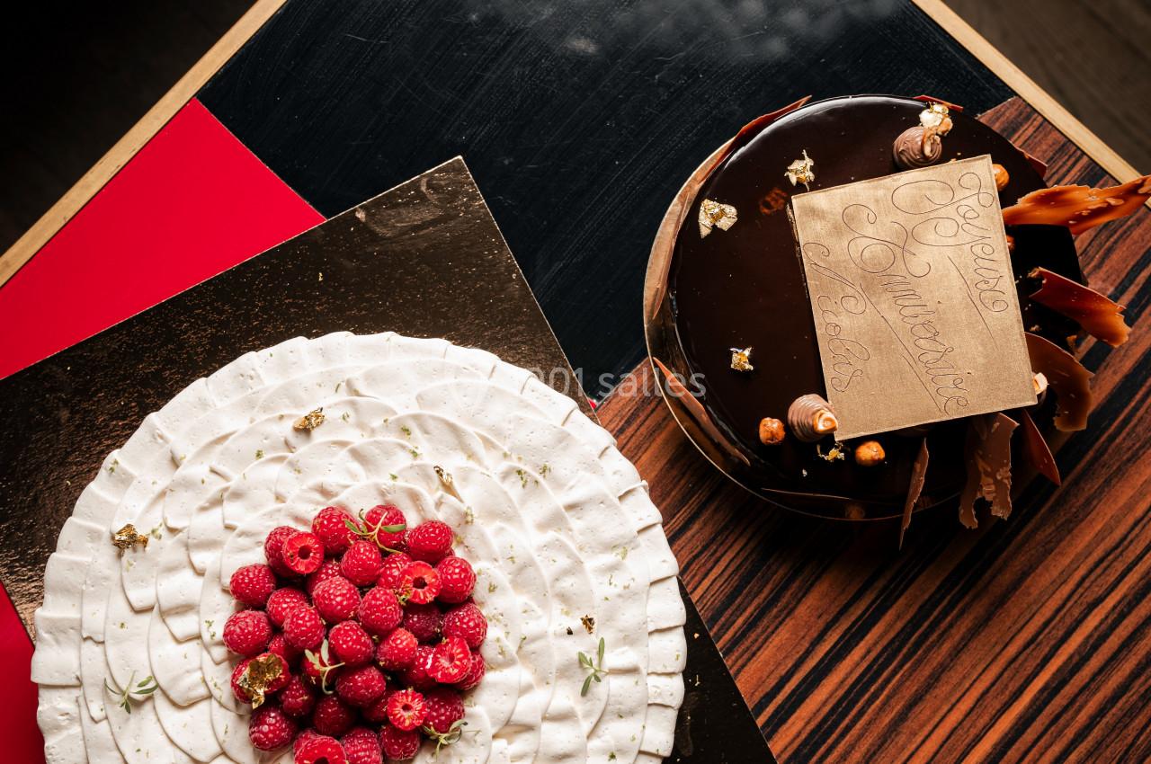 Deux gâteaux décorés, l'un avec des framboises et l'autre avec un glaçage chocolat et une plaque en chocolat dorée.