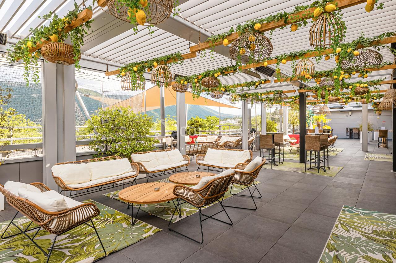 Terrasse aménagée avec mobilier en rotin, plantes suspendues et vue sur un paysage montagneux en arrière-plan.