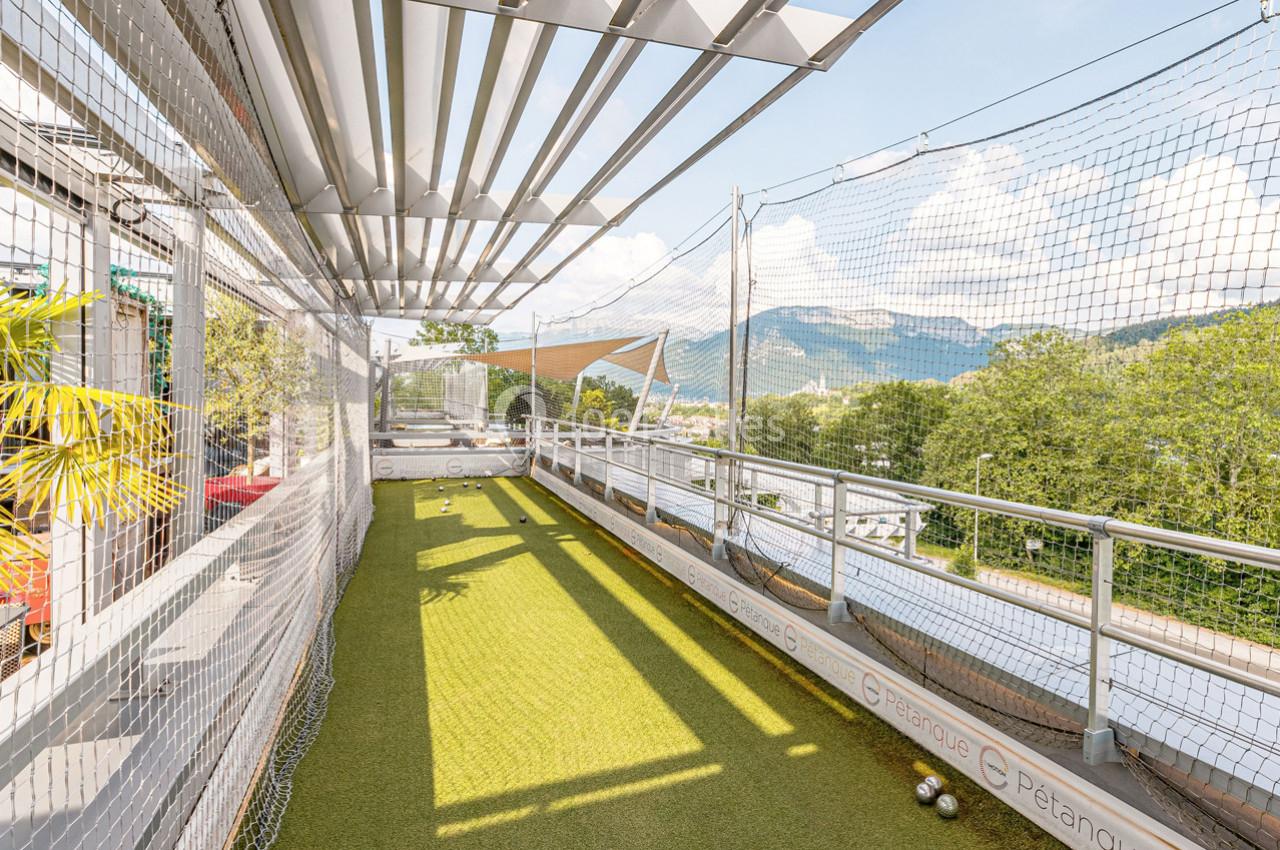 Terrain de pétanque extérieur sur une terrasse, entouré de filets, avec vue sur des collines et un ciel dégagé.
