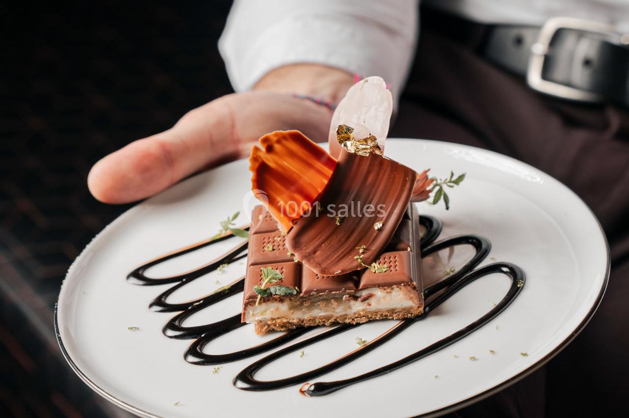 Assiette de dessert avec chocolat, décorations en caramel et sauce au chocolat, tenue par une personne en chemise blanche.