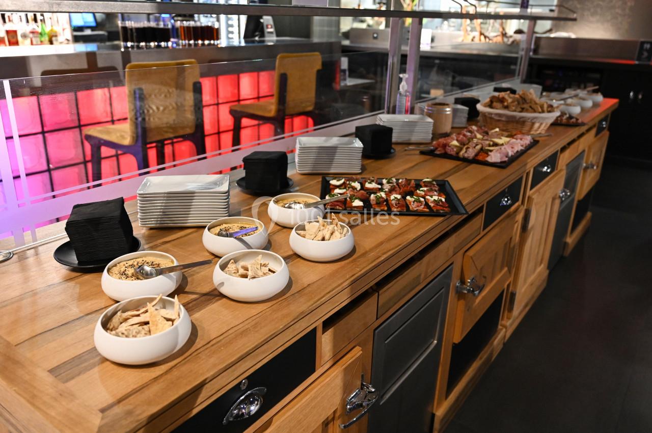 Buffet avec assiettes, bols de snacks, toasts garnis et viennoiseries sur un comptoir en bois dans un restaurant.