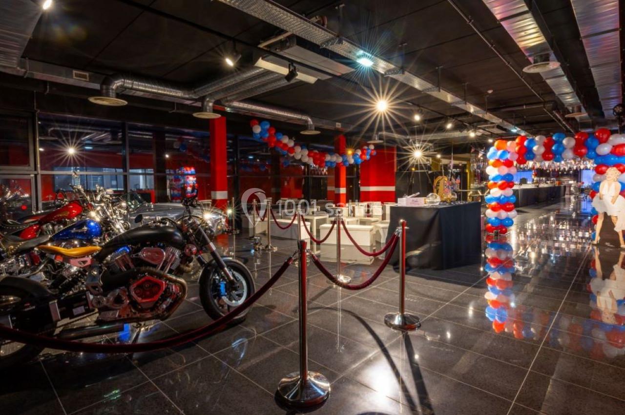 Salle décorée avec des ballons rouges et bleus, motos exposées et espace aménagé pour un événement.