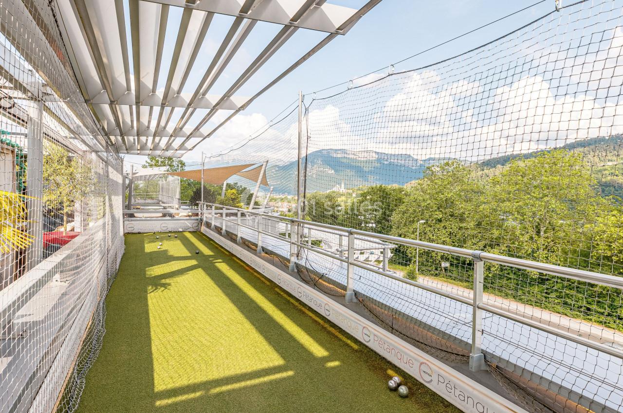 Terrain de pétanque en plein air sur une terrasse avec vue sur des montagnes et un ciel dégagé.