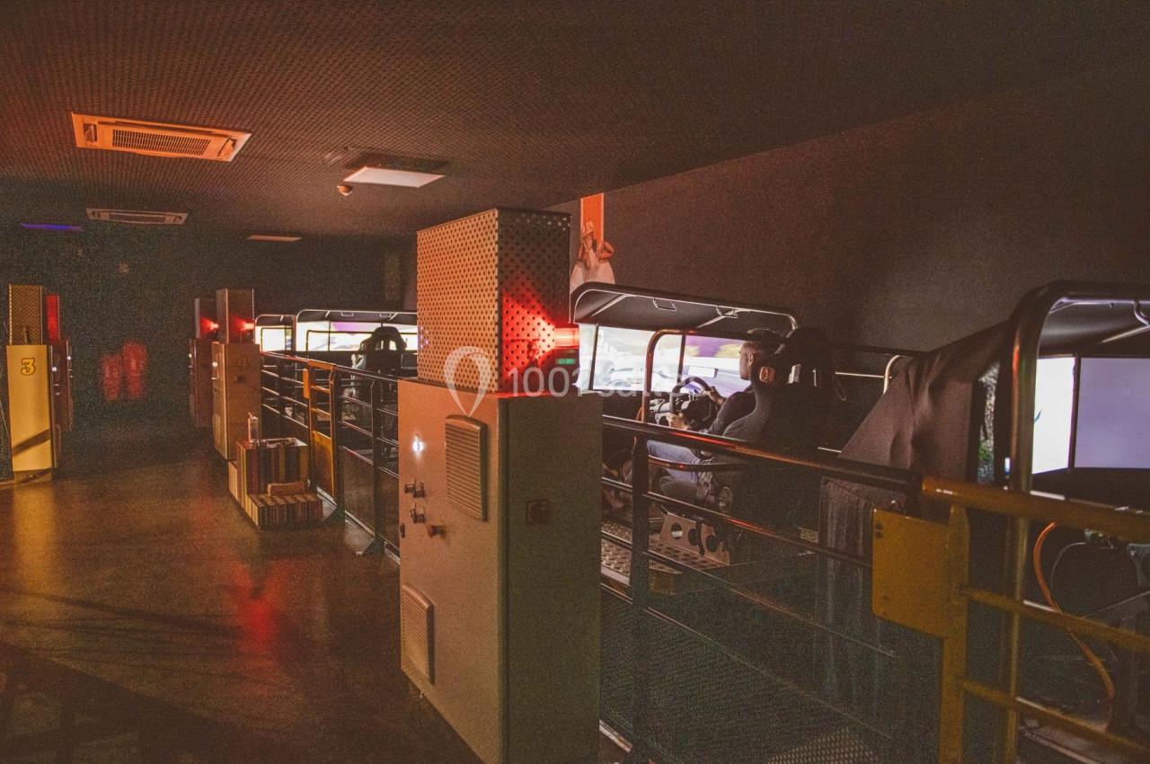 Des simulateurs de conduite alignés dans une salle sombre, avec des écrans lumineux et des sièges équipés de volants.