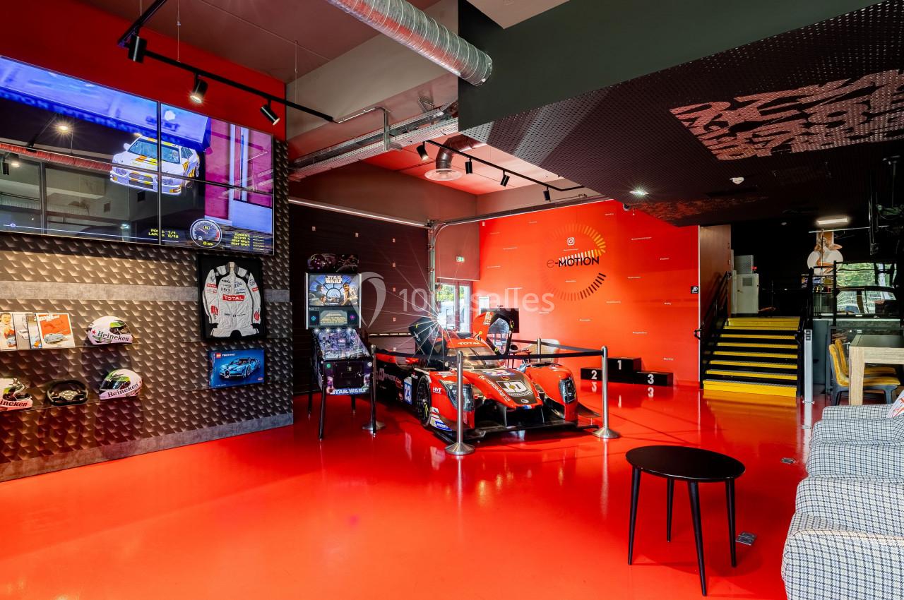 Salle immersive avec simulateur de course, écrans, casques exposés et décorations sur le thème de l'automobile.