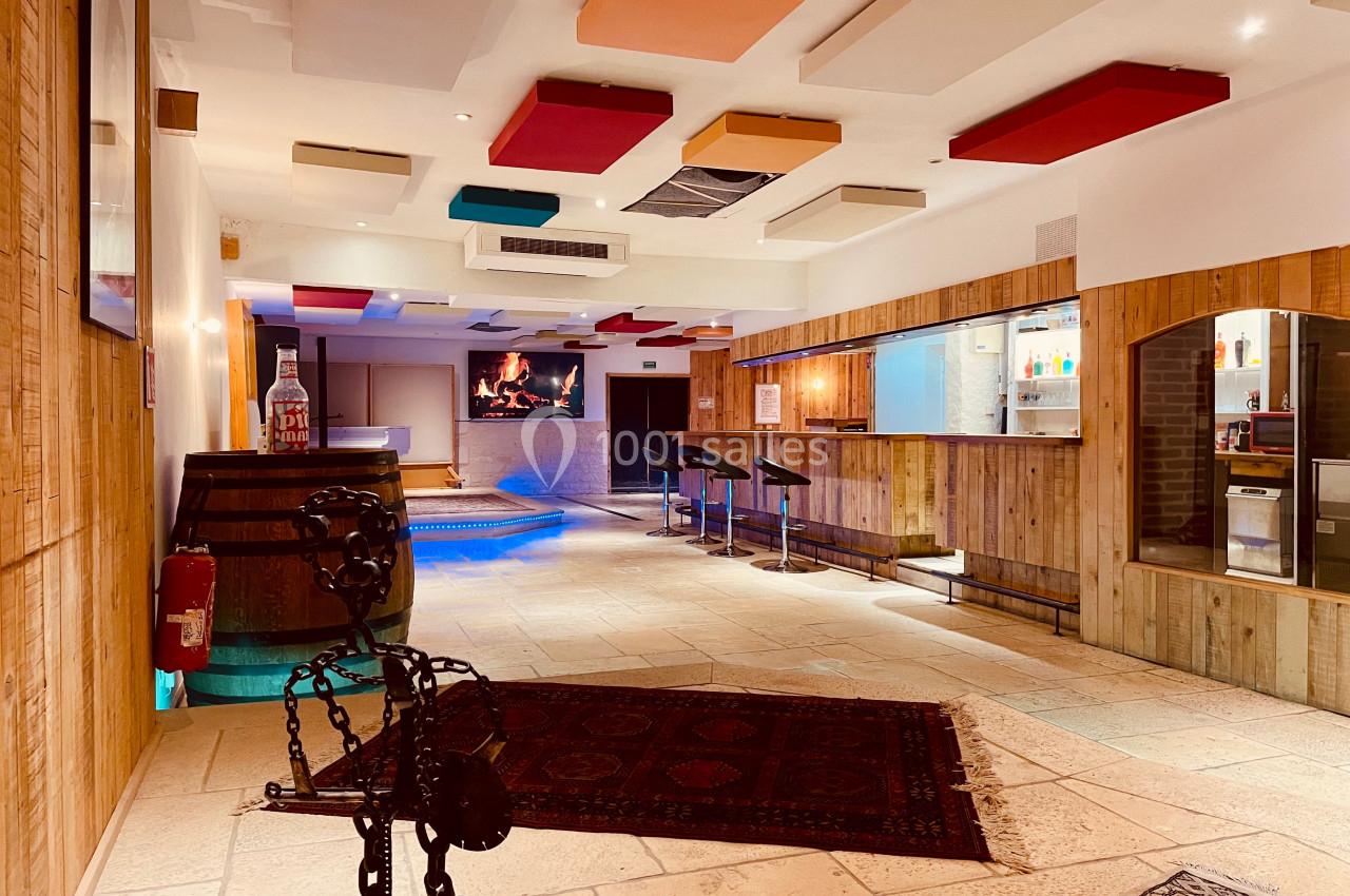 Intérieur d'un espace avec bar en bois, plafond coloré, cheminée allumée et éclairage chaleureux.