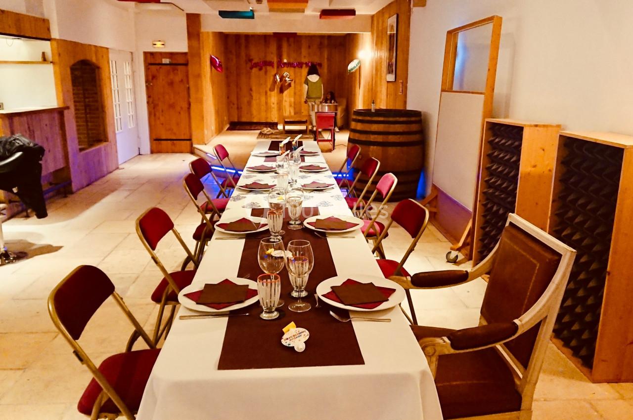 Salle aménagée avec une longue table dressée pour un repas, entourée de chaises pliantes et décorée sobrement.