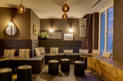 Salon cosy avec tables rondes, tabourets noirs, coussins décoratifs et éclairage tamisé près de grandes fenêtres.