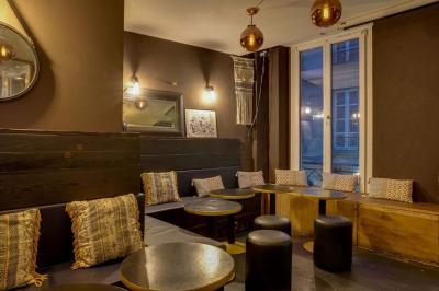 Salon cosy avec tables rondes, tabourets noirs, coussins décoratifs et éclairage tamisé près de grandes fenêtres.