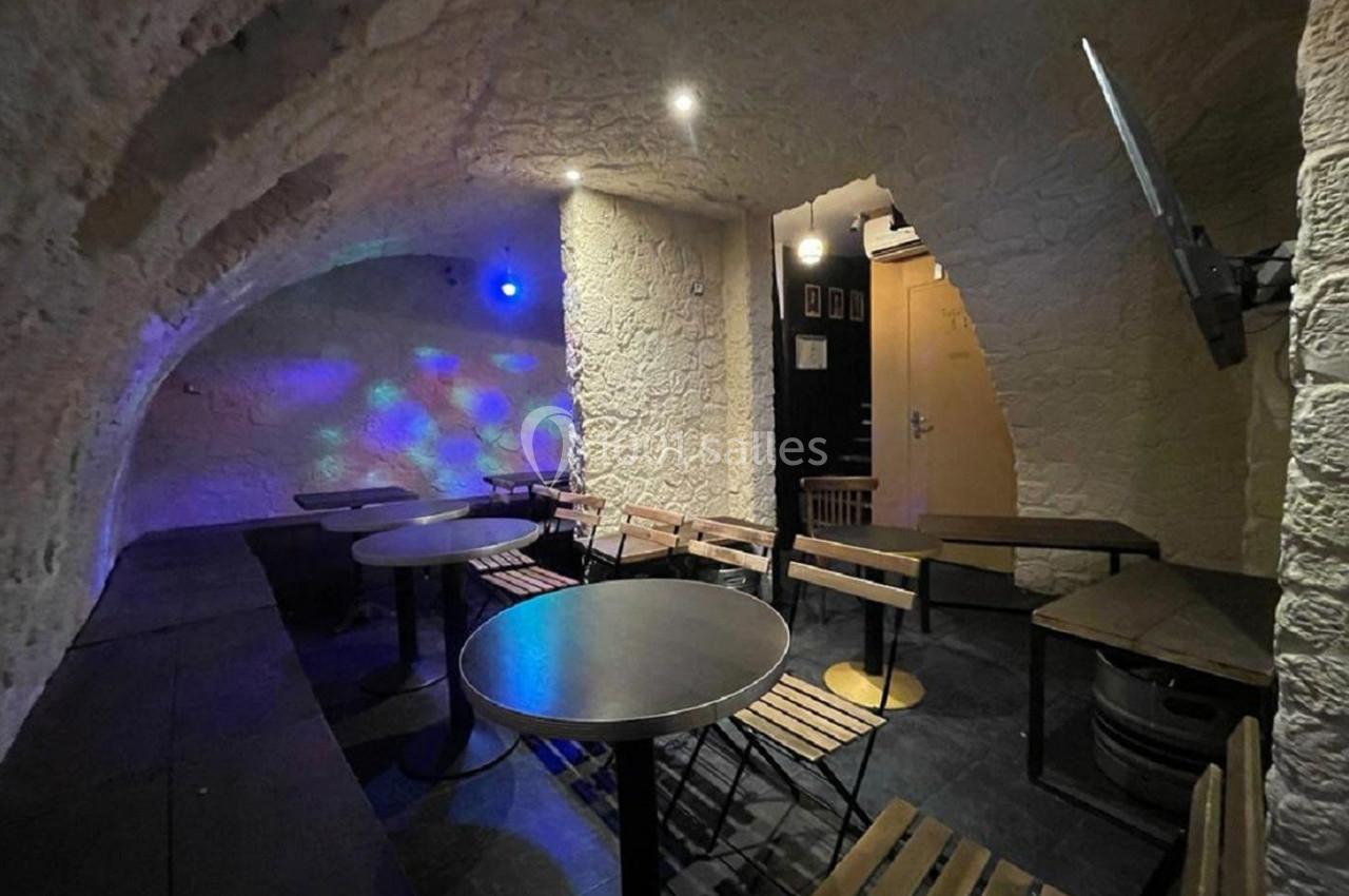 Salle voûtée en pierre avec tables, chaises en bois et éclairage tamisé, décorée de points lumineux colorés.