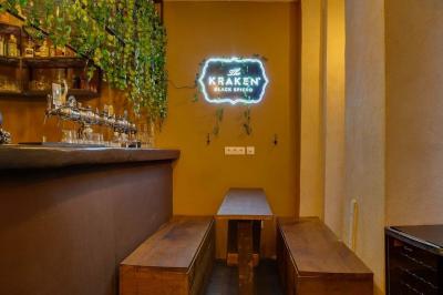 Bar avec comptoir en bois, étagères de bouteilles, plantes suspendues et enseigne lumineuse murale.