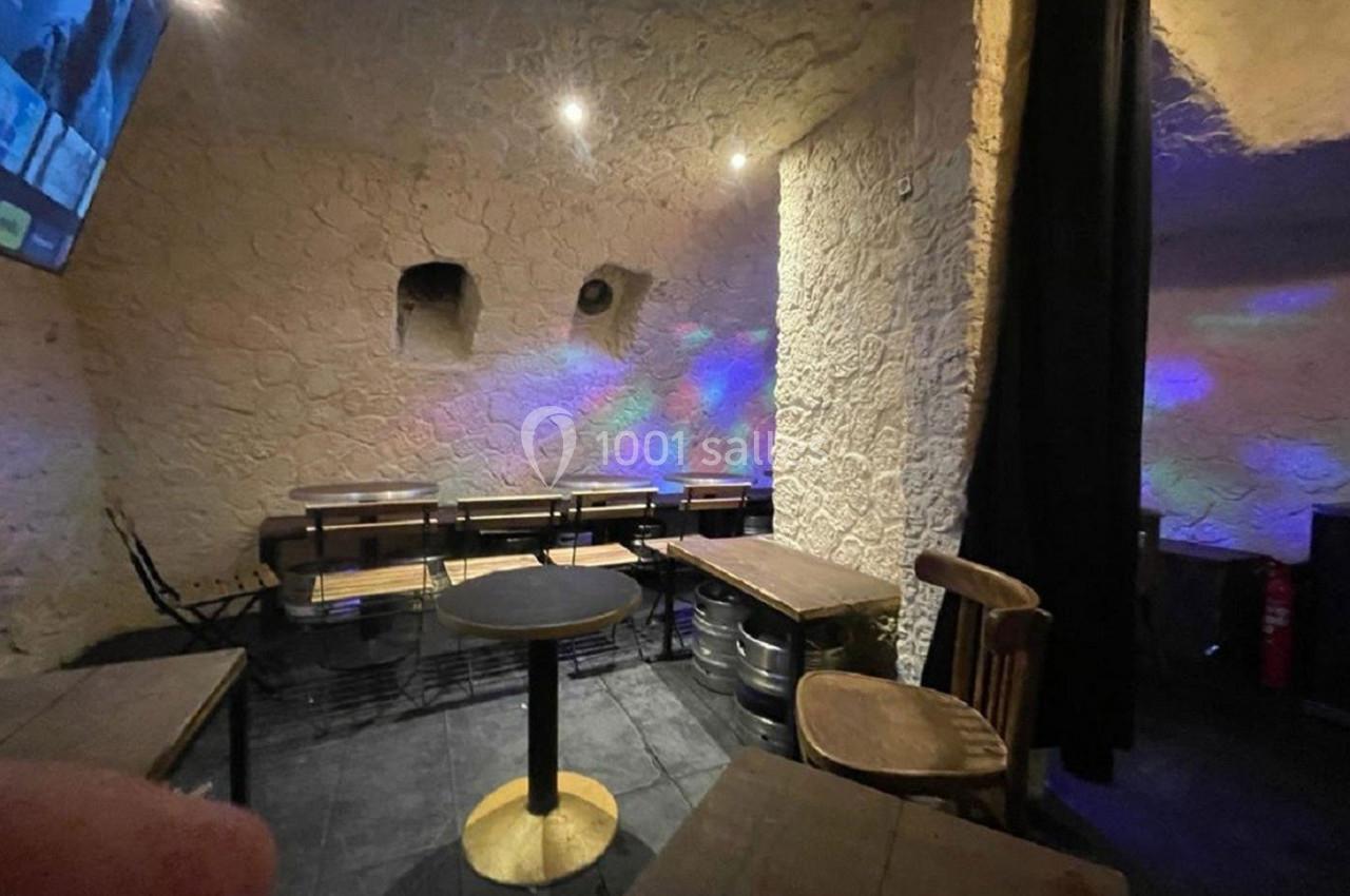 Salle avec murs en pierre, tables en bois, chaises simples et éclairage tamisé avec reflets colorés.