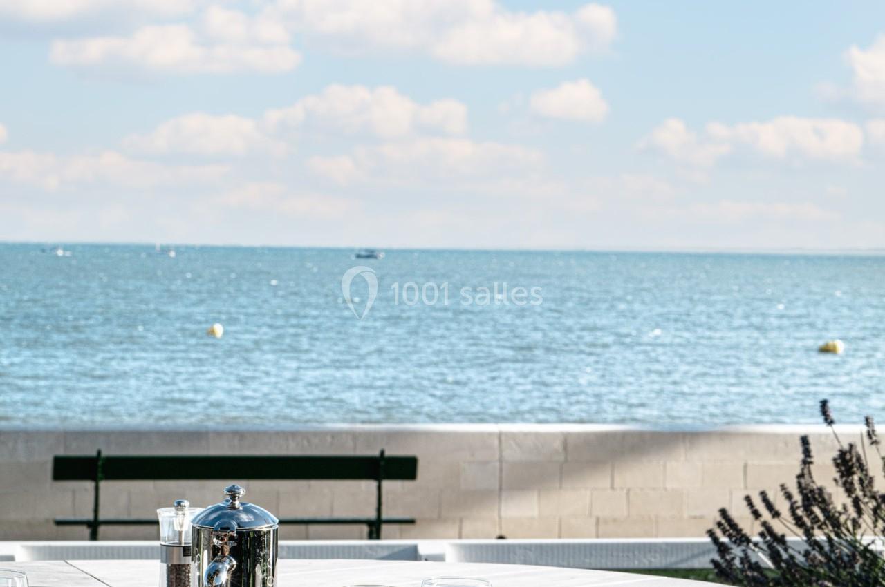 Table dressée pour un petit-déjeuner en extérieur avec vue sur la mer, sous un ciel bleu parsemé de nuages.