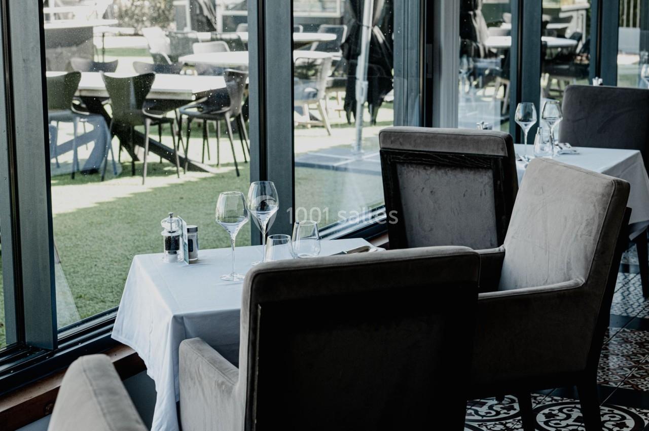 Salle de restaurant élégante avec tables dressées, grandes baies vitrées et vue sur une terrasse extérieure.