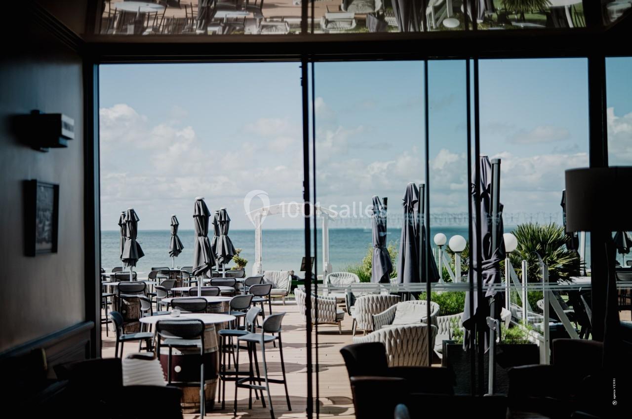 Terrasse d'un restaurant avec des tables et parasols, donnant sur une vue dégagée sur la mer et un ciel partiellement…