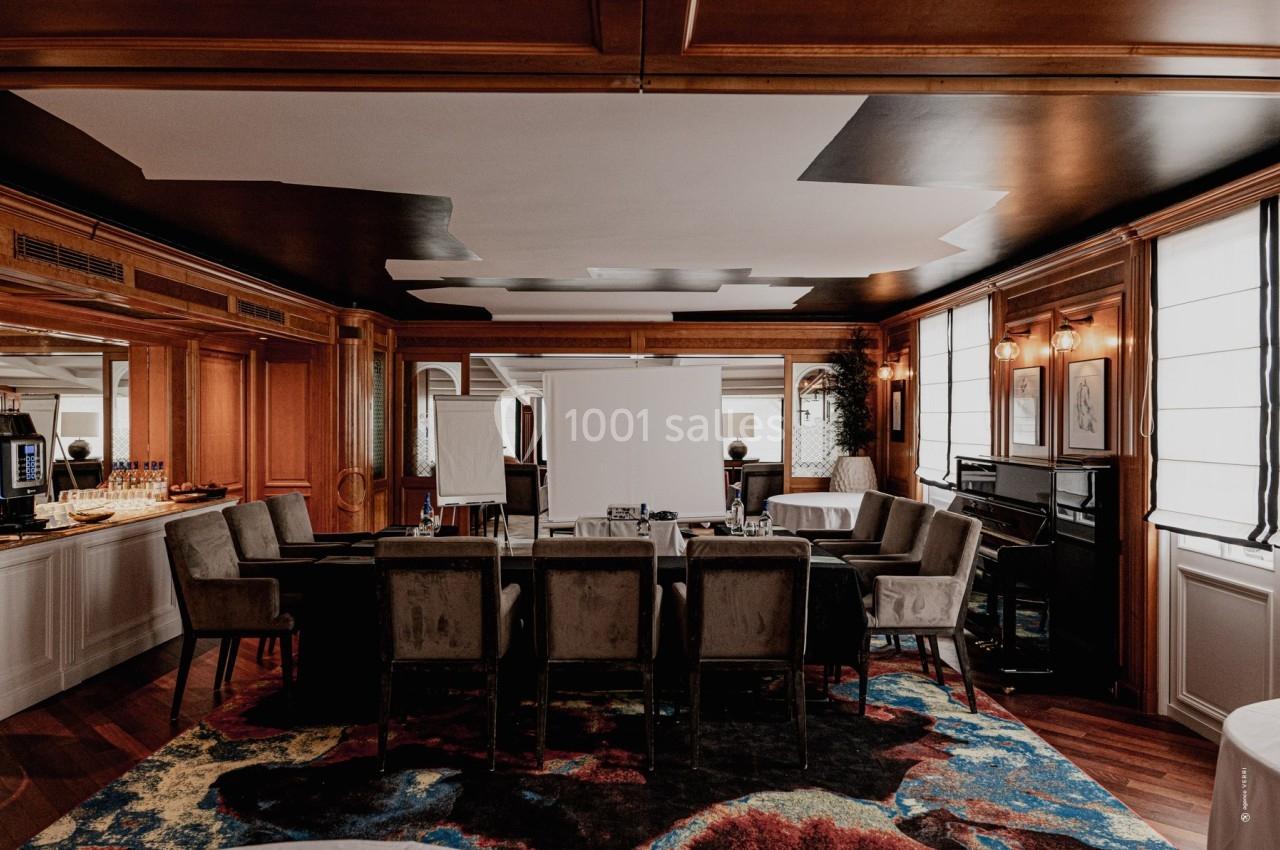 Salle de réunion élégante avec table rectangulaire, chaises en velours, éclairage tamisé et décorations en bois.