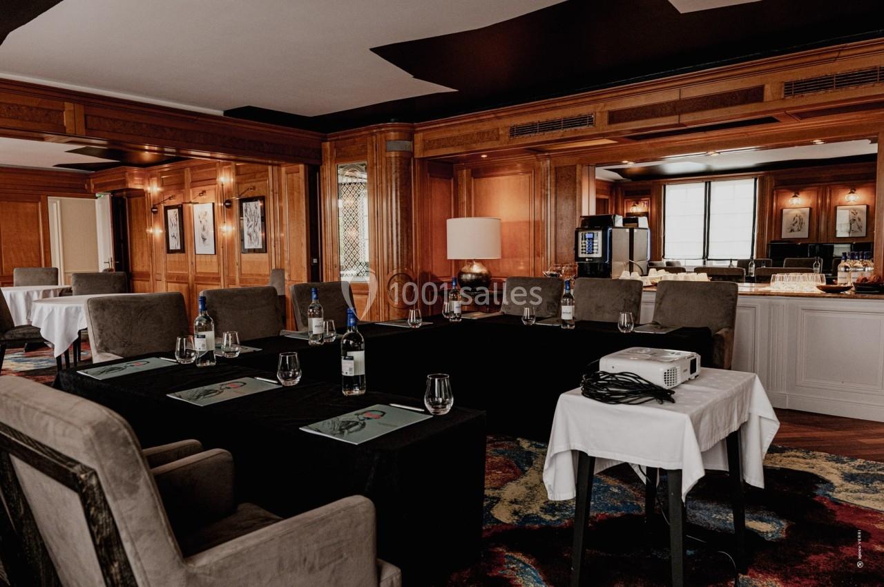 Salle de réunion élégante avec tables disposées en U, chaises rembourrées, projecteur et buffet en arrière-plan.