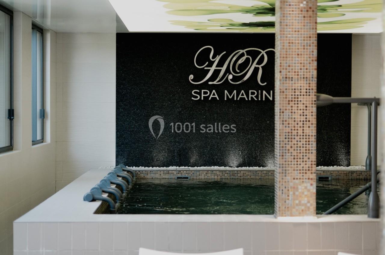 Piscine intérieure d'un spa avec mosaïques, jets d'eau et mur noir portant l'inscription ’HR Spa Marin’.