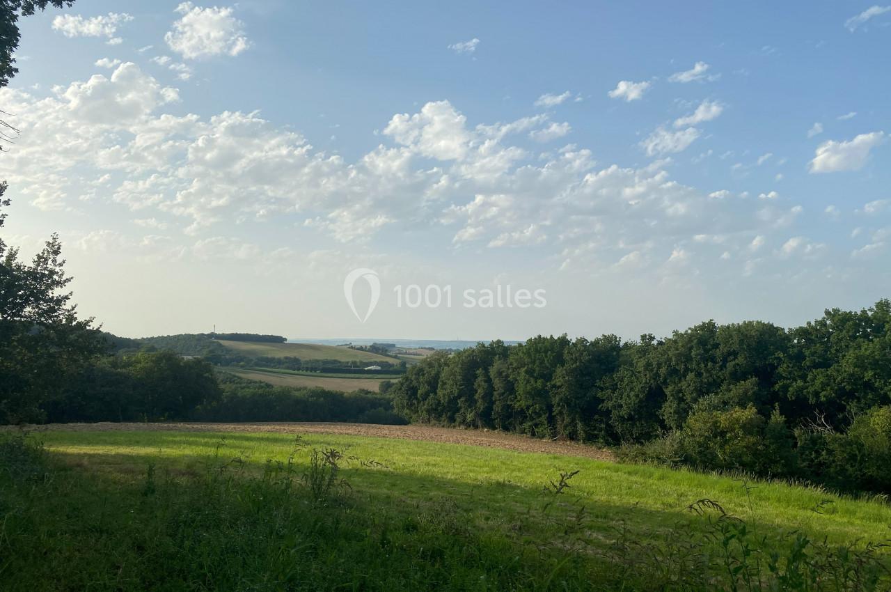 Paysage champêtre avec une prairie verdoyante, des arbres en bordure et un horizon dégagé sous un ciel partiellement nuageux.