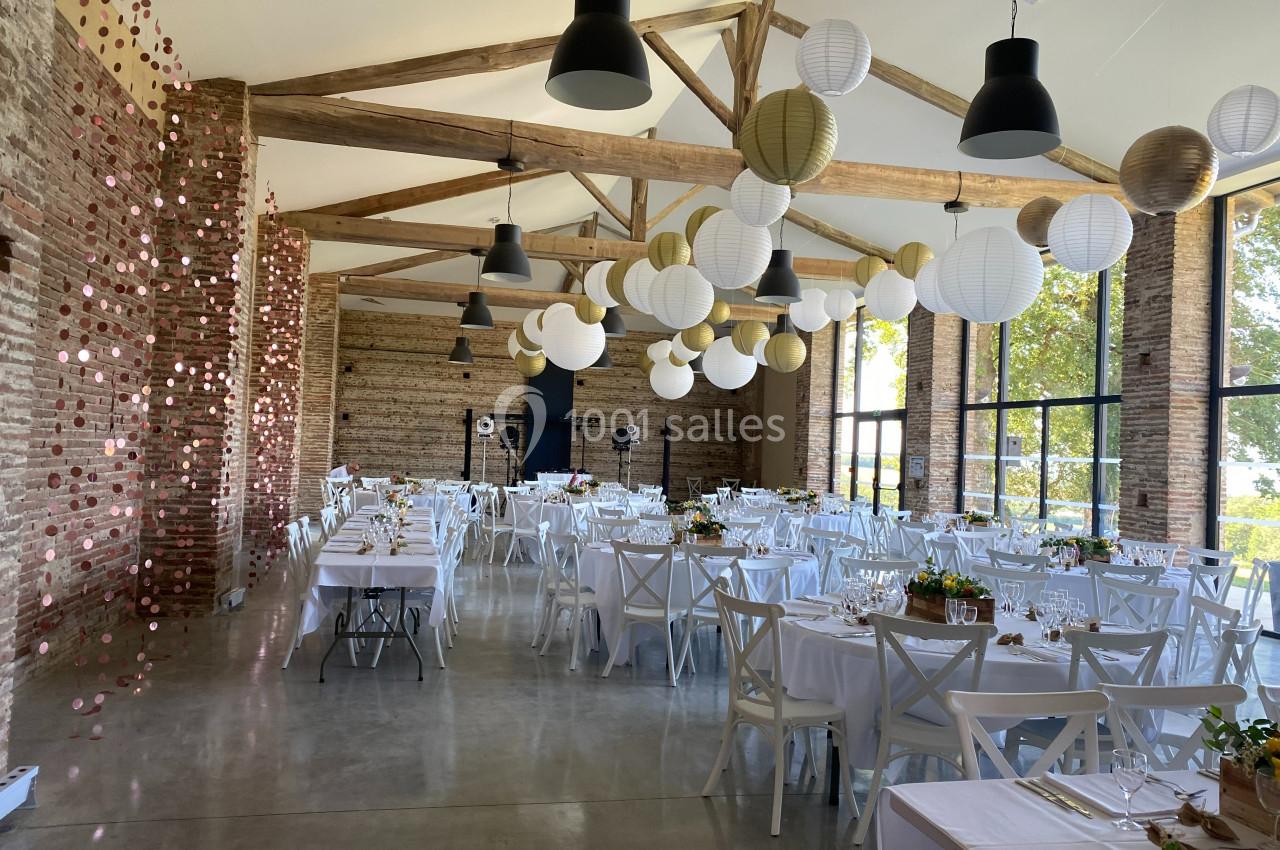 Salle de réception lumineuse avec tables dressées, décorations suspendues et murs en briques apparentes.